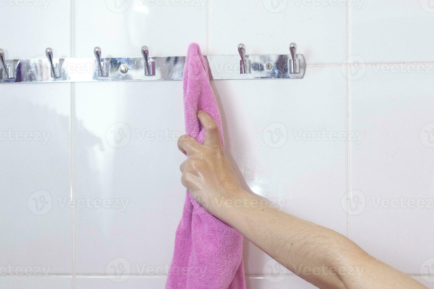 jovem fêmea depois de banho. mulher molhado mão levando dela Rosa roupão de banho suspensão em uma gancho. levando roupão de banho depois de chuveiro foto