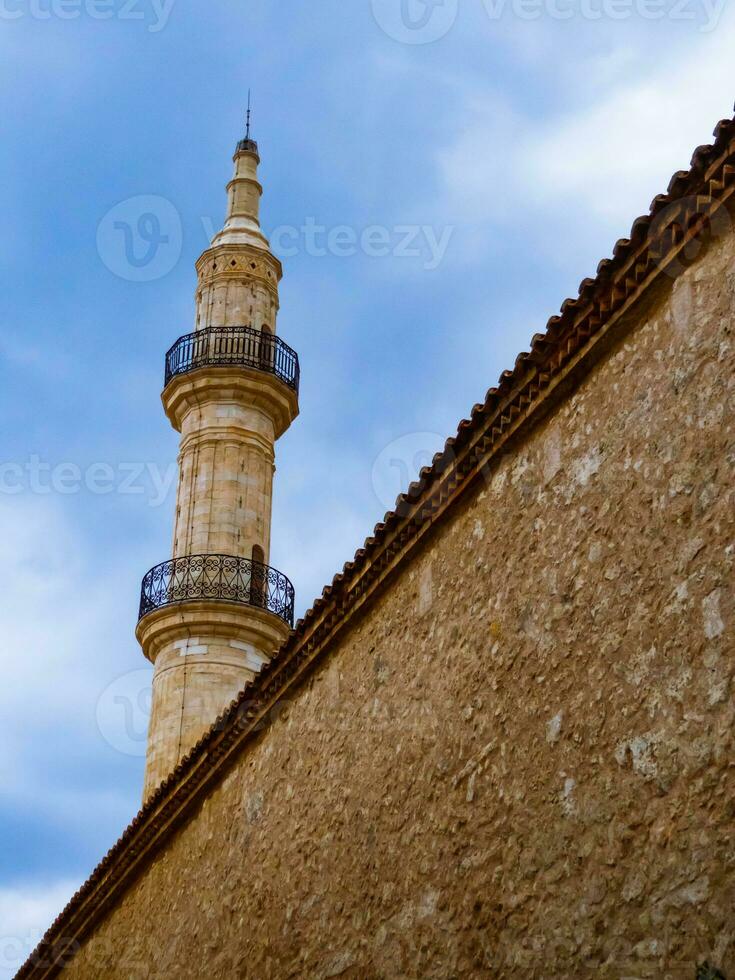 minarete do medieval mesquita imponente sobre a parede dentro a velho parte do rethymno - Creta, Grécia foto