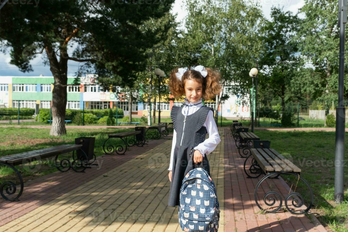 alegre engraçado menina com uma desdentado sorrir dentro uma escola uniforme com branco arcos dentro escola quintal. costas para escola, setembro 1. feliz aluno com uma mochila. primário Educação, elementar aula. foto