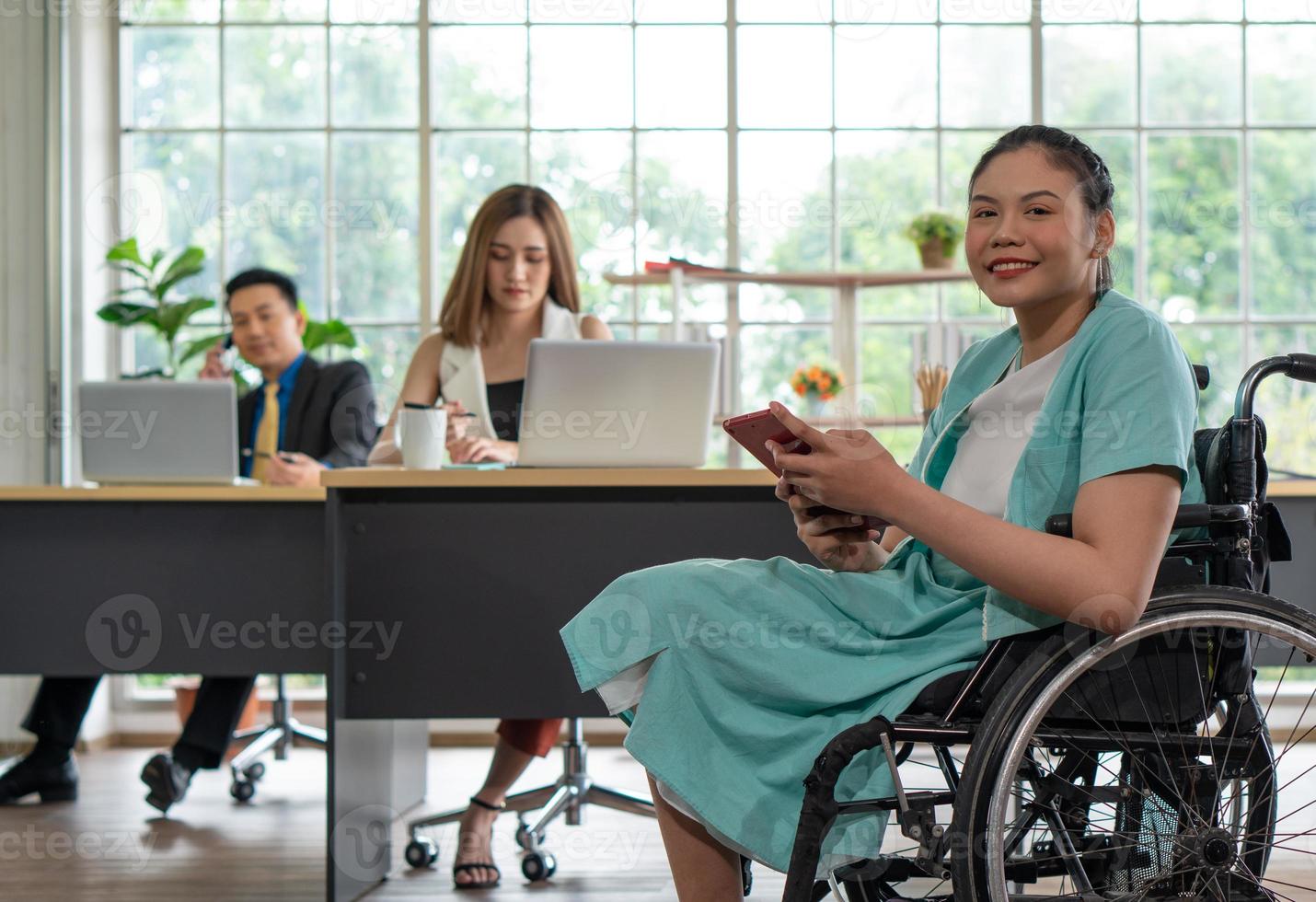 jovem mulher com deficiência sentada em cadeira de rodas com colegas no escritório foto