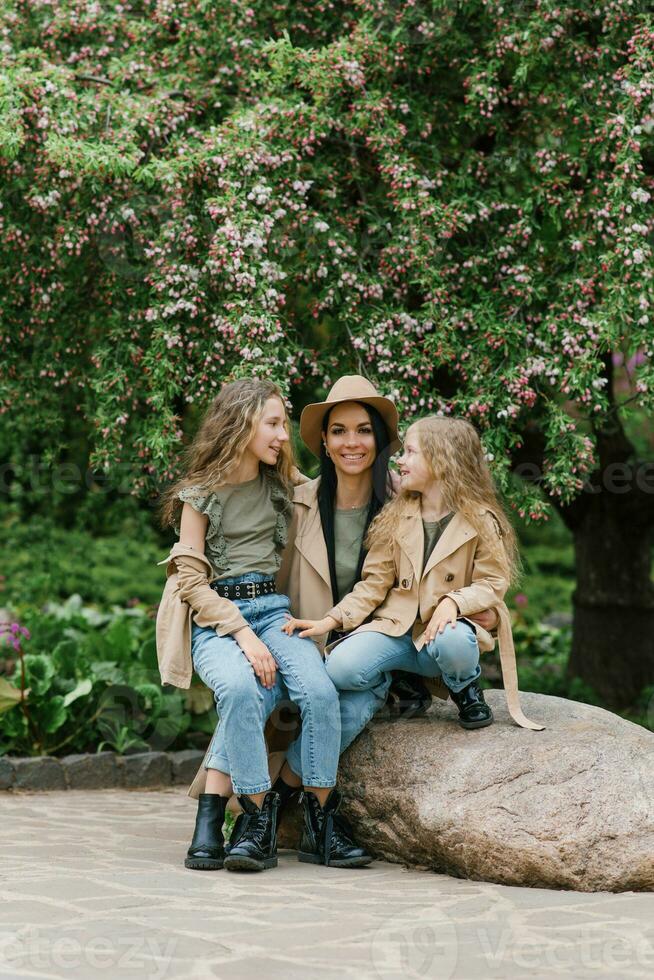 à moda caucasiano mãe e dela dois filhas estão conversando e caminhando dentro uma Primavera florescendo parque. mãe dia e uma feliz família foto