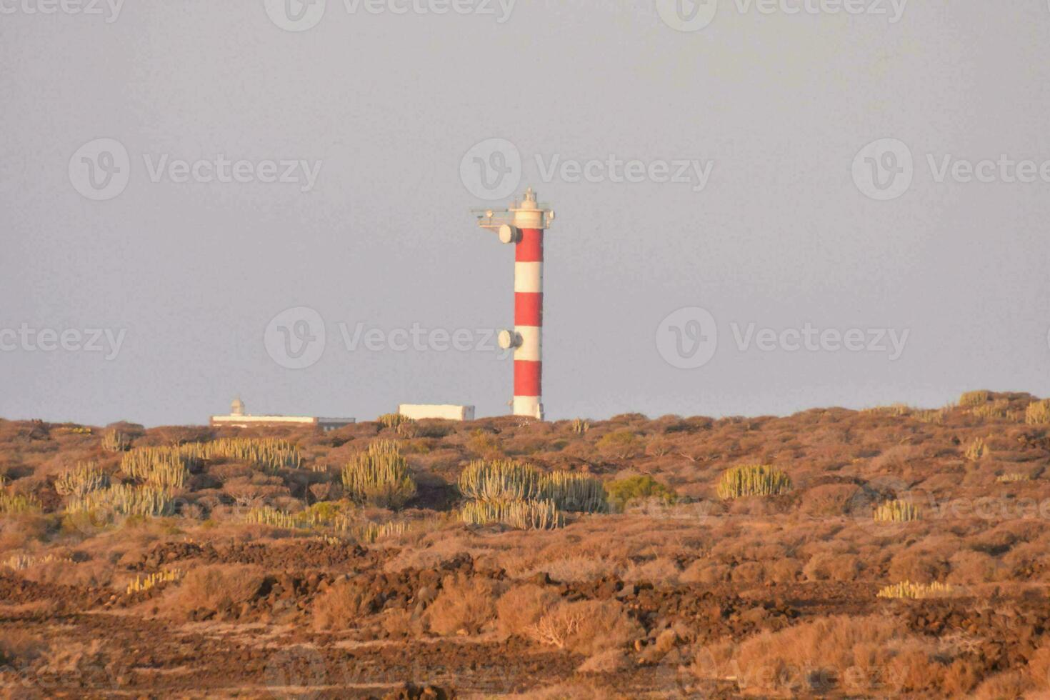 uma farol em uma Colina com uma vermelho e branco torre foto