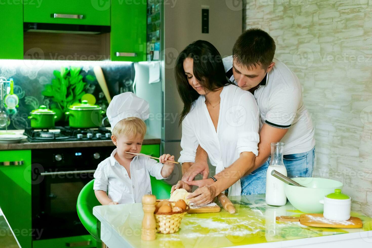 feliz família mãe e pequeno filho e Papai estão preparando massa dentro cozinha às mesa. produtos para massa estão em mesa foto