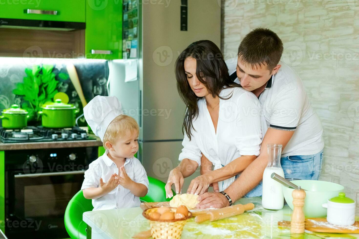 feliz família mãe e pequeno filho e Papai estão preparando massa dentro cozinha às mesa. produtos para massa estão em mesa foto