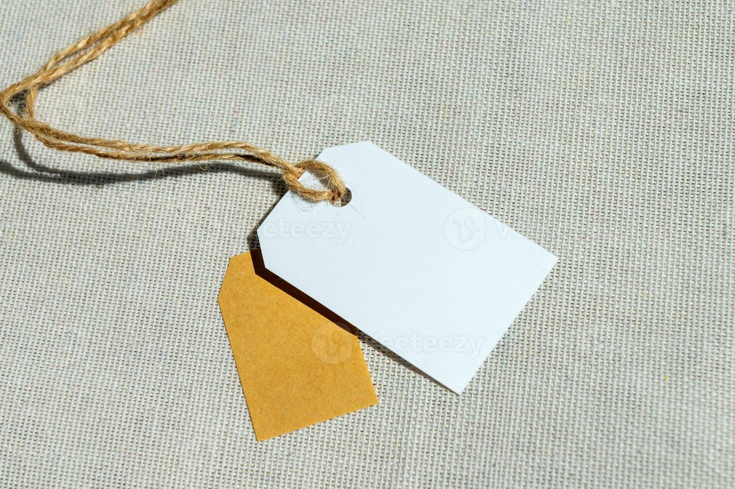 dois retangular Tag com uma corda em uma cinzento tecido. em branco rótulo brincar com preço tag foto