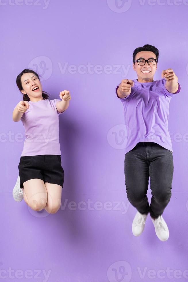 jovem casal asiático pulando no fundo roxo foto