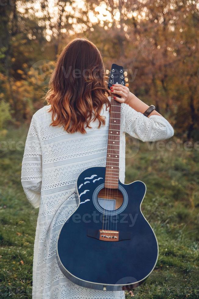 vista traseira de uma jovem segurando uma guitarra no parque ao pôr do sol foto