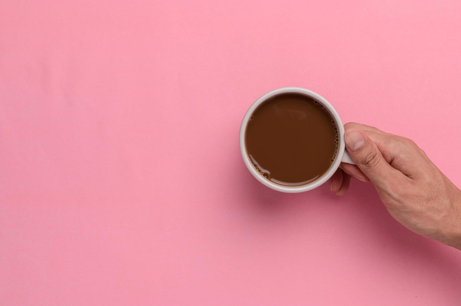 mão segurando uma caneca de café em um fundo rosa foto