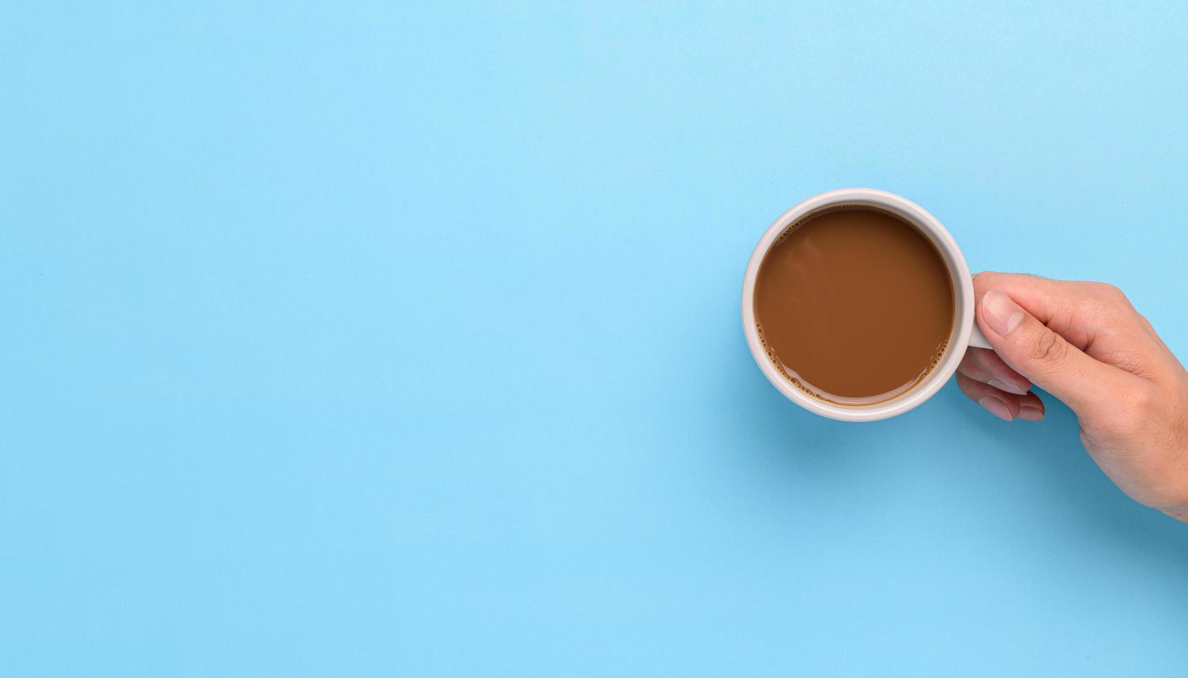 mão segurando uma caneca de café em um fundo azul foto