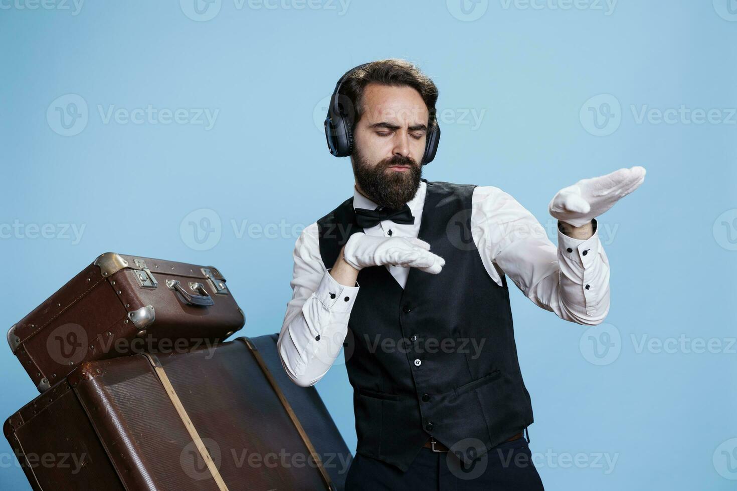 hotel funcionários membro dançando em Câmera, tendo Diversão com música em fones de ouvido enquanto ele desgasta elegante roupas e luvas. jovem homem trabalhador com audio fone de ouvido sentindo-me confiante ou engraçado. foto