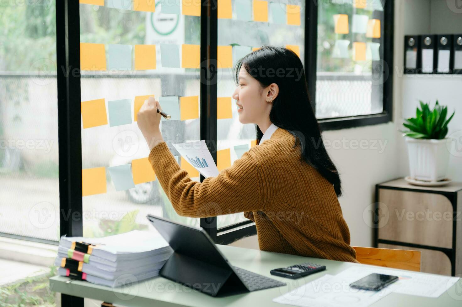 ásia empresária segurando uma caneta levando Nota em papel de nota em anexo para uma espelho Como uma lembrete computador portátil e tábua em a desk.in escritório foto