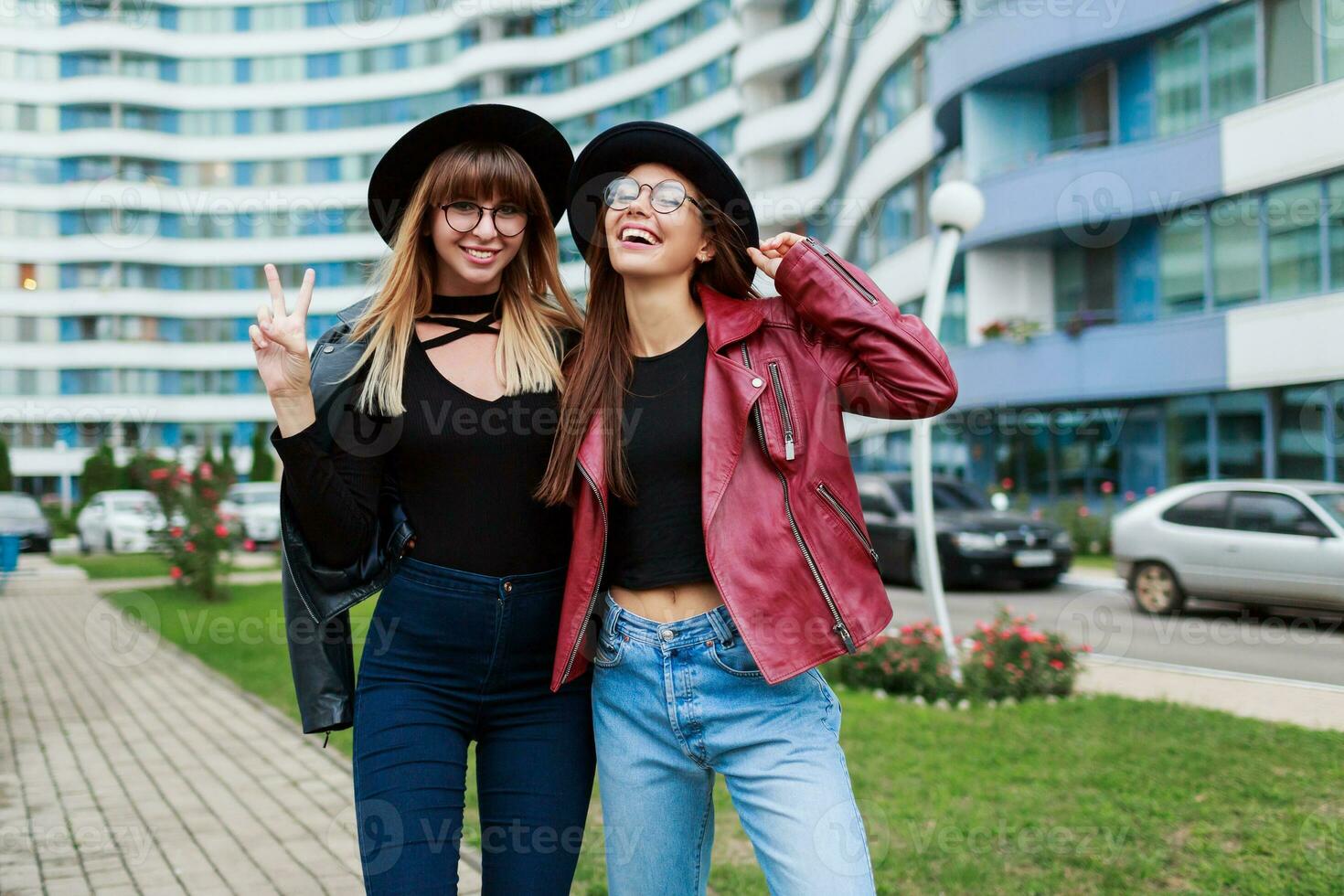 outono moda olhar. casal do atraente gracioso meninas dentro fofa volta óculos e Preto chapéus posando em fundo do o negócio Centro. foto