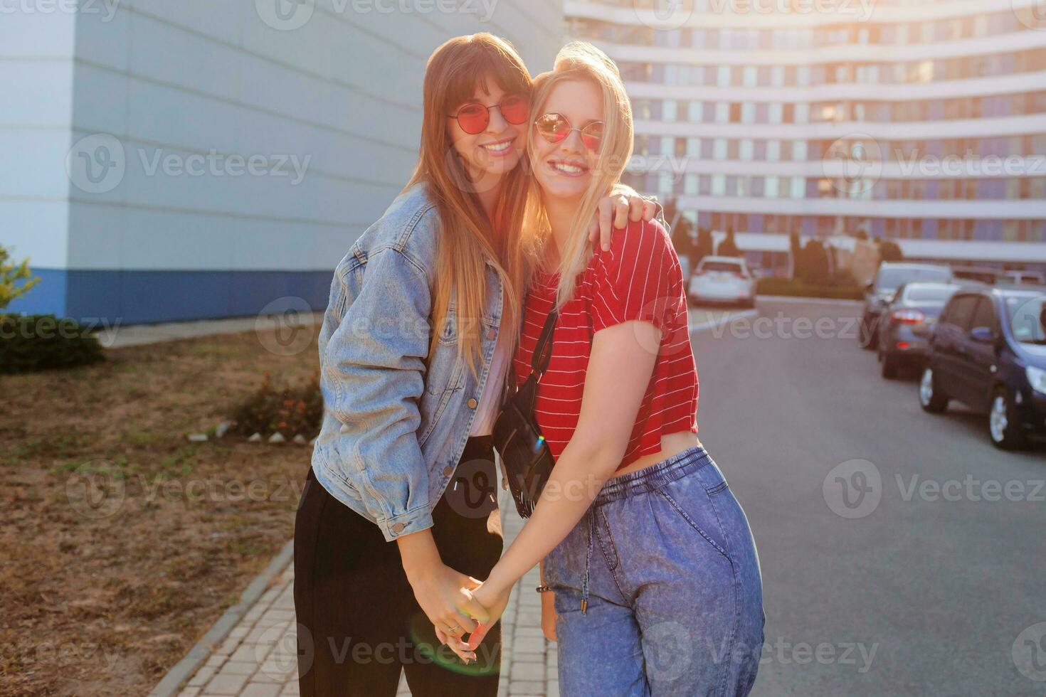 dois alegre mulheres tendo Diversão ar livre. à moda jeans Jaqueta com imprimir. urbano fundo . foto