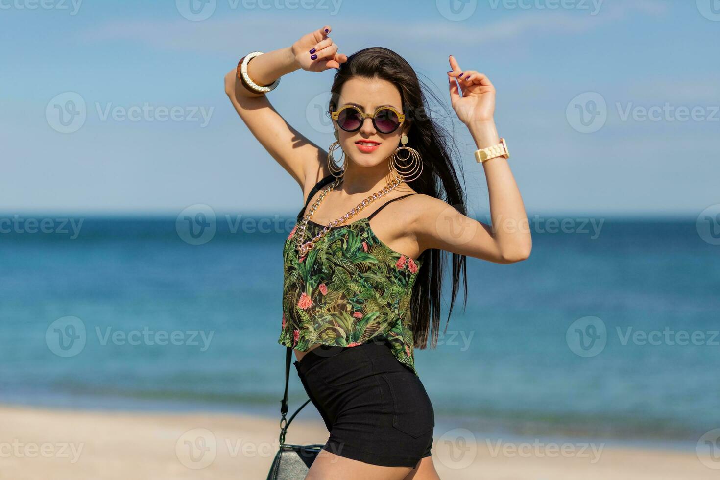 verão retrato do à moda mulher com grande na moda acessórios e brincos posando em a de praia. sexy corpo. menina dançando e tendo Diversão. foto
