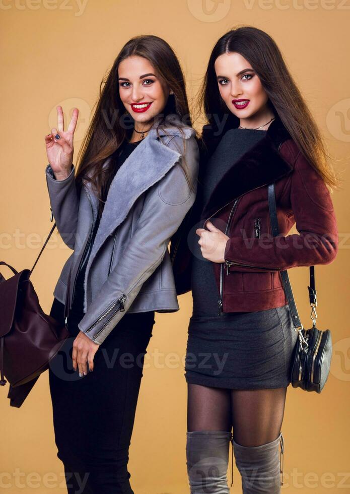 fechar acima estilo de vida retrato do dois garotas, melhor amigos dentro inverno ou outono roupas posando dentro estúdio em bege fundo. elegante casual jaqueta. foto