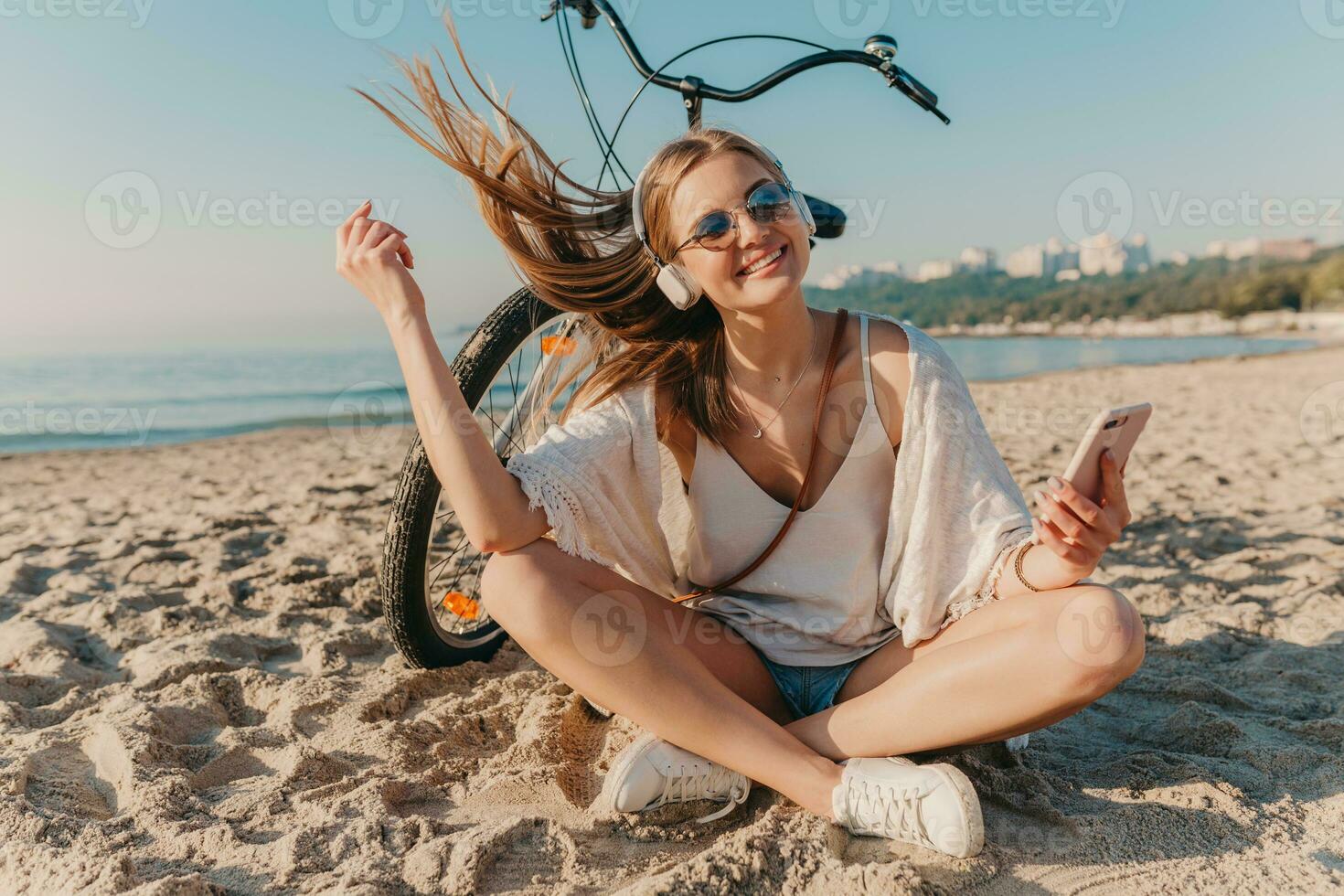 jovem atraente loiro sorridente mulher em período de férias sentado em de praia foto