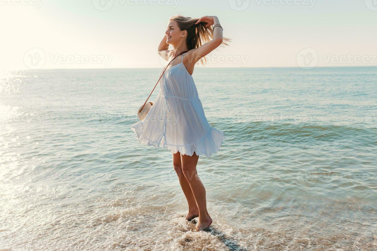 jovem atraente feliz mulher dançando girando por aí de mar de praia dentro branco vestir período de férias foto