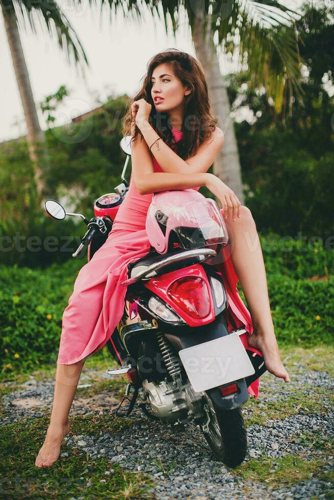 jovem à moda sexy lindo mulher dentro Rosa vestir em lambreta moto tropical período de férias foto