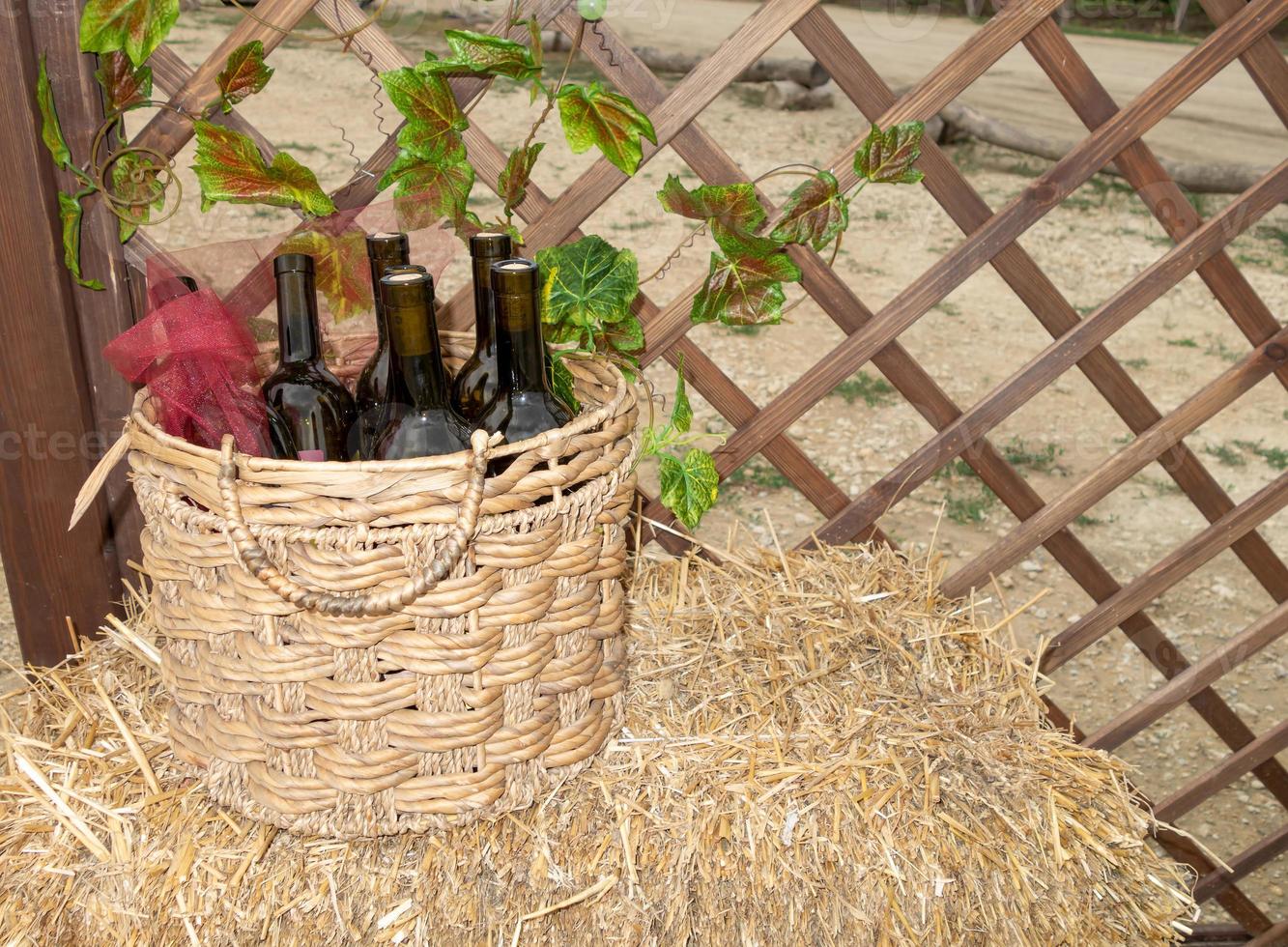 garrafas de vinho em uma cesta de palha em um canudo perto de uma treliça de madeira foto