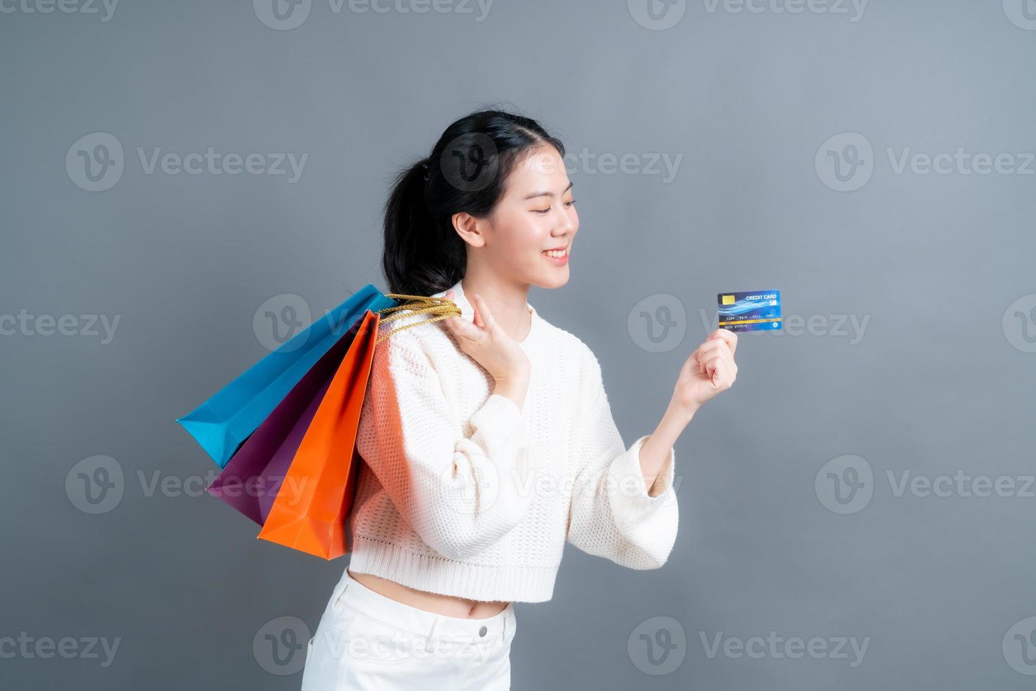 linda mulher asiática com sacolas de compras e apresentando cartão de crédito foto
