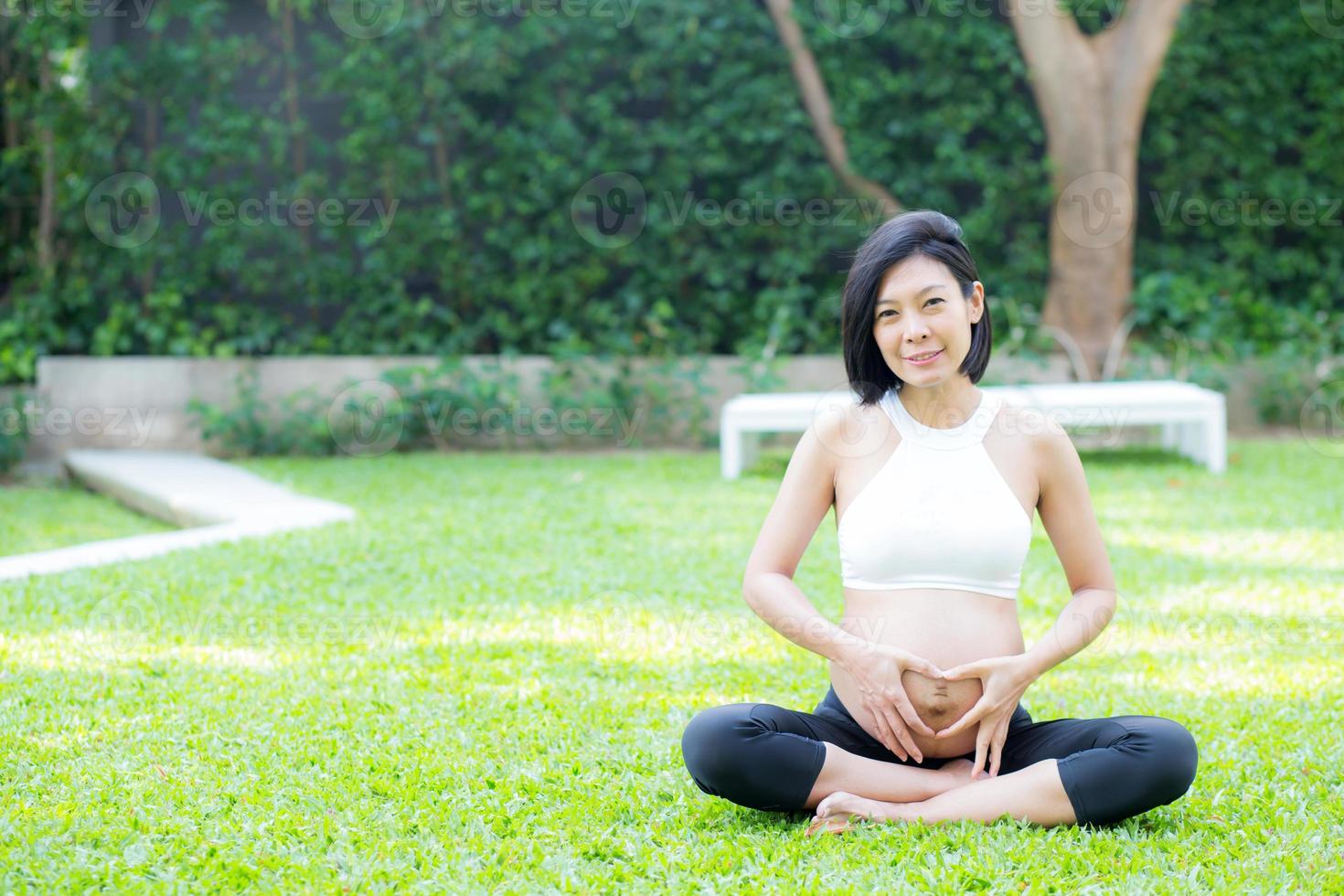 mulher grávida feliz com gesto de mão em forma de coração no parque foto