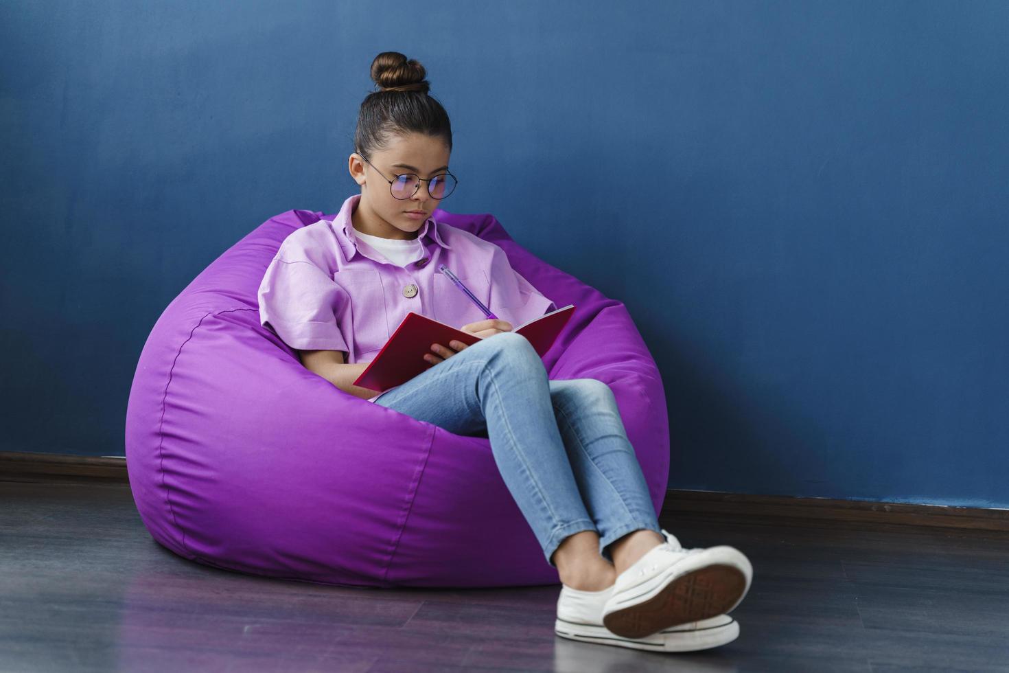 focada e fofa adolescente sentada em um pufe roxo, estudando foto