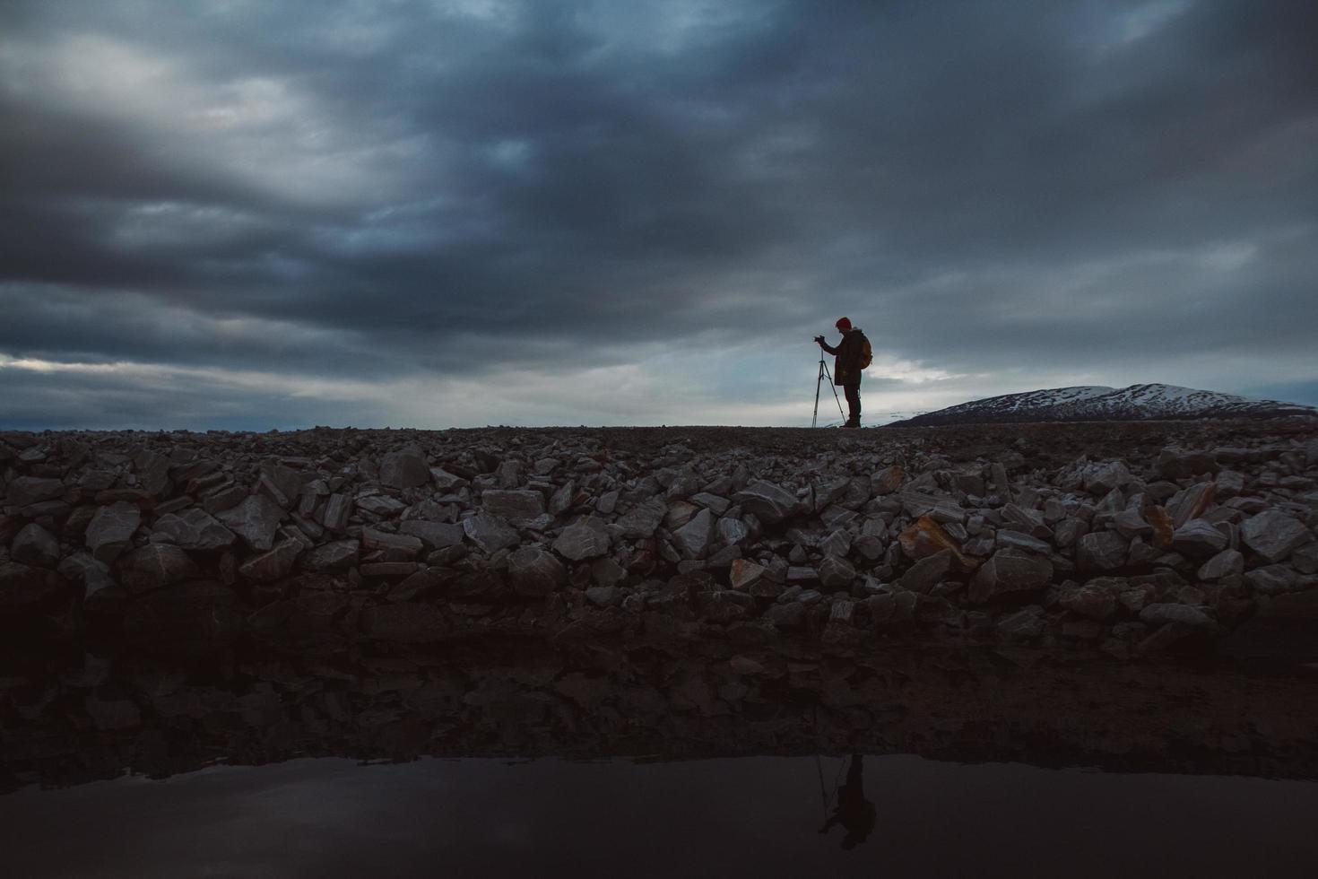 silhueta de um fotógrafo ou viajante com um tripé sobre uma pedra foto