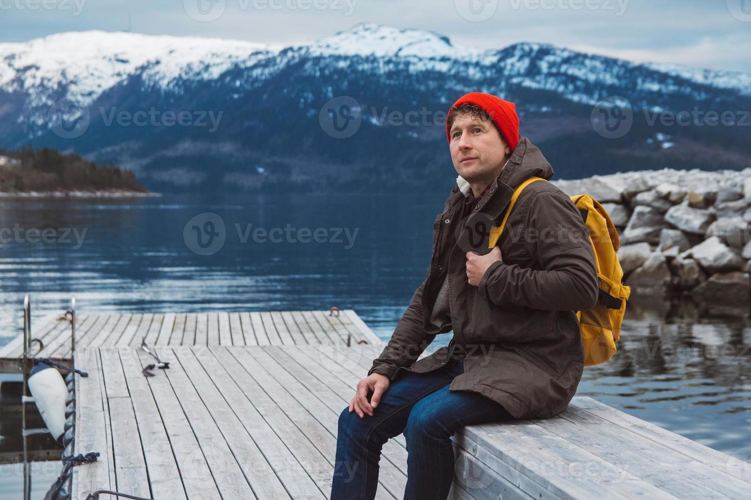 homem sentado no cais de madeira no fundo da montanha e do lago foto