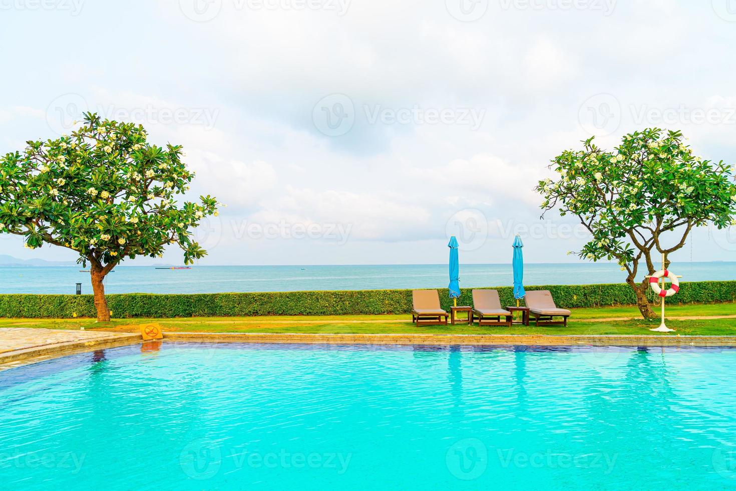 cadeira de piscina e guarda-sol ao redor da piscina com fundo do mar foto