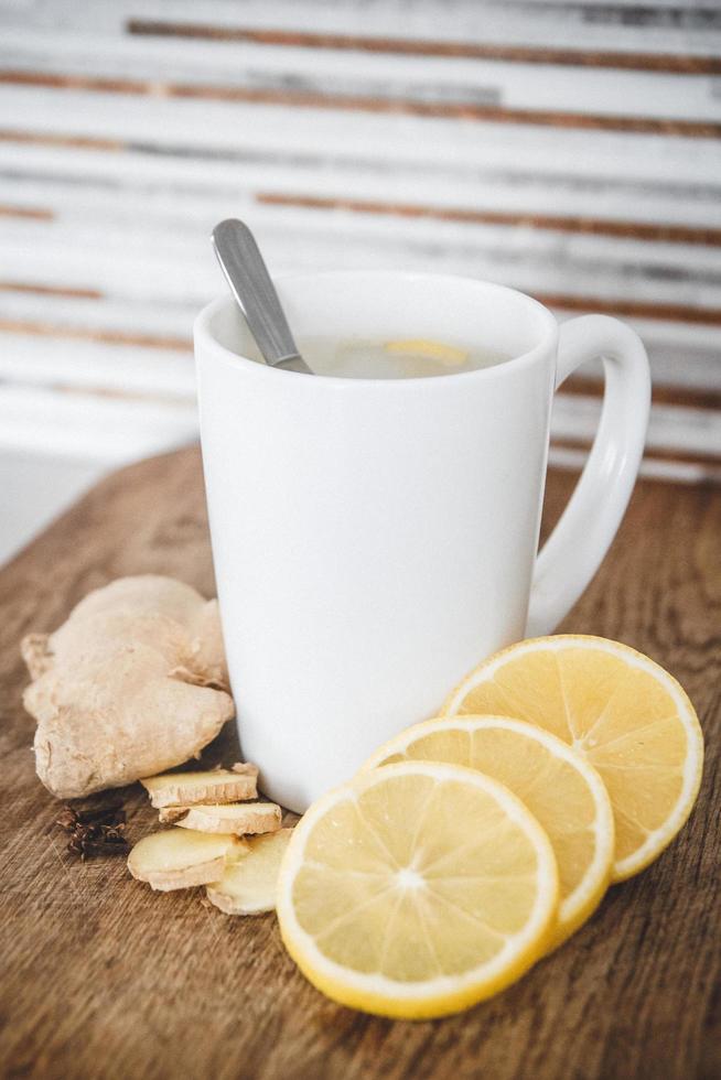 chá quente de gengibre com limão em uma xícara branca na mesa de madeira foto