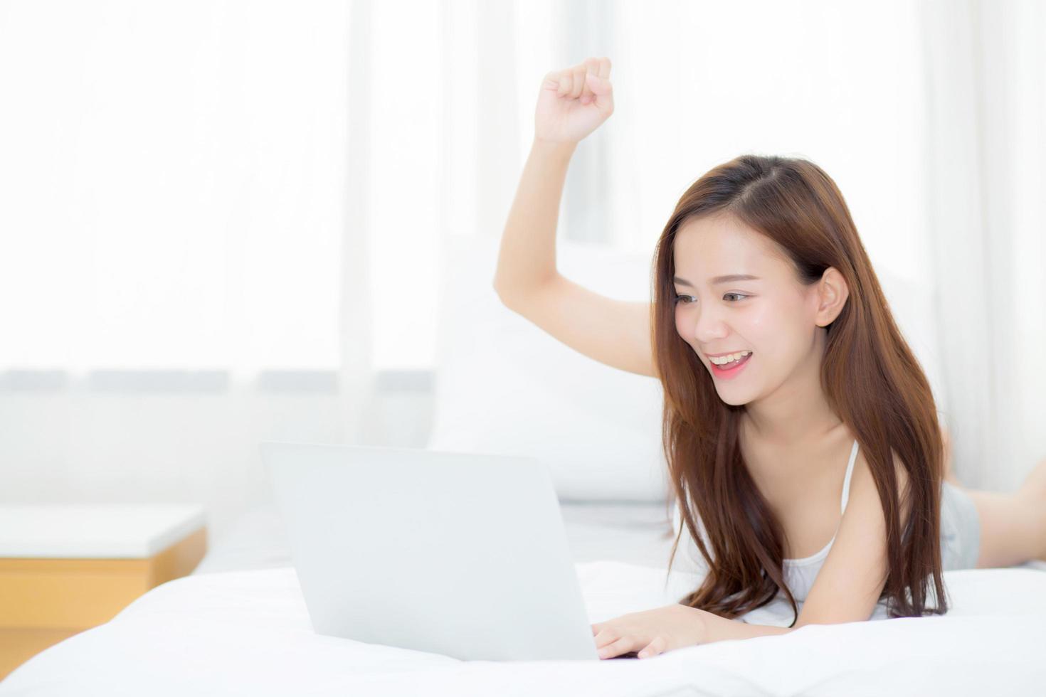 jovem mulher asiática relaxando e relaxando com o laptop na cama foto