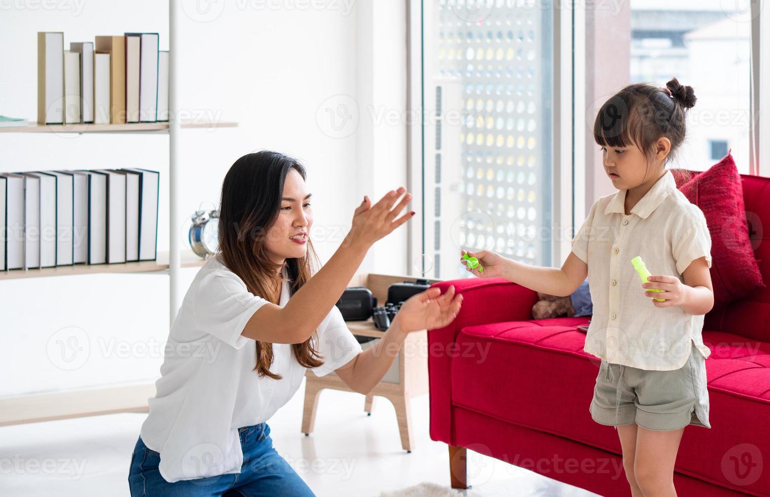 Mãe asiática jogando bolhas com a criança na sala de estar foto