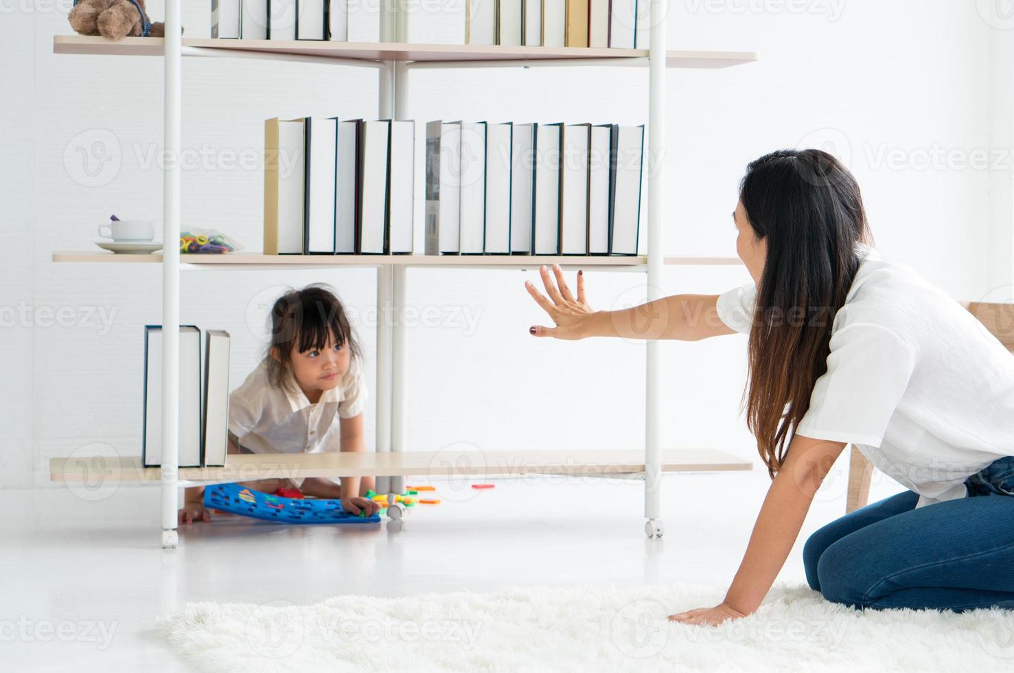 menina asiática brincando de esconde-esconde com a mãe na sala de estar foto