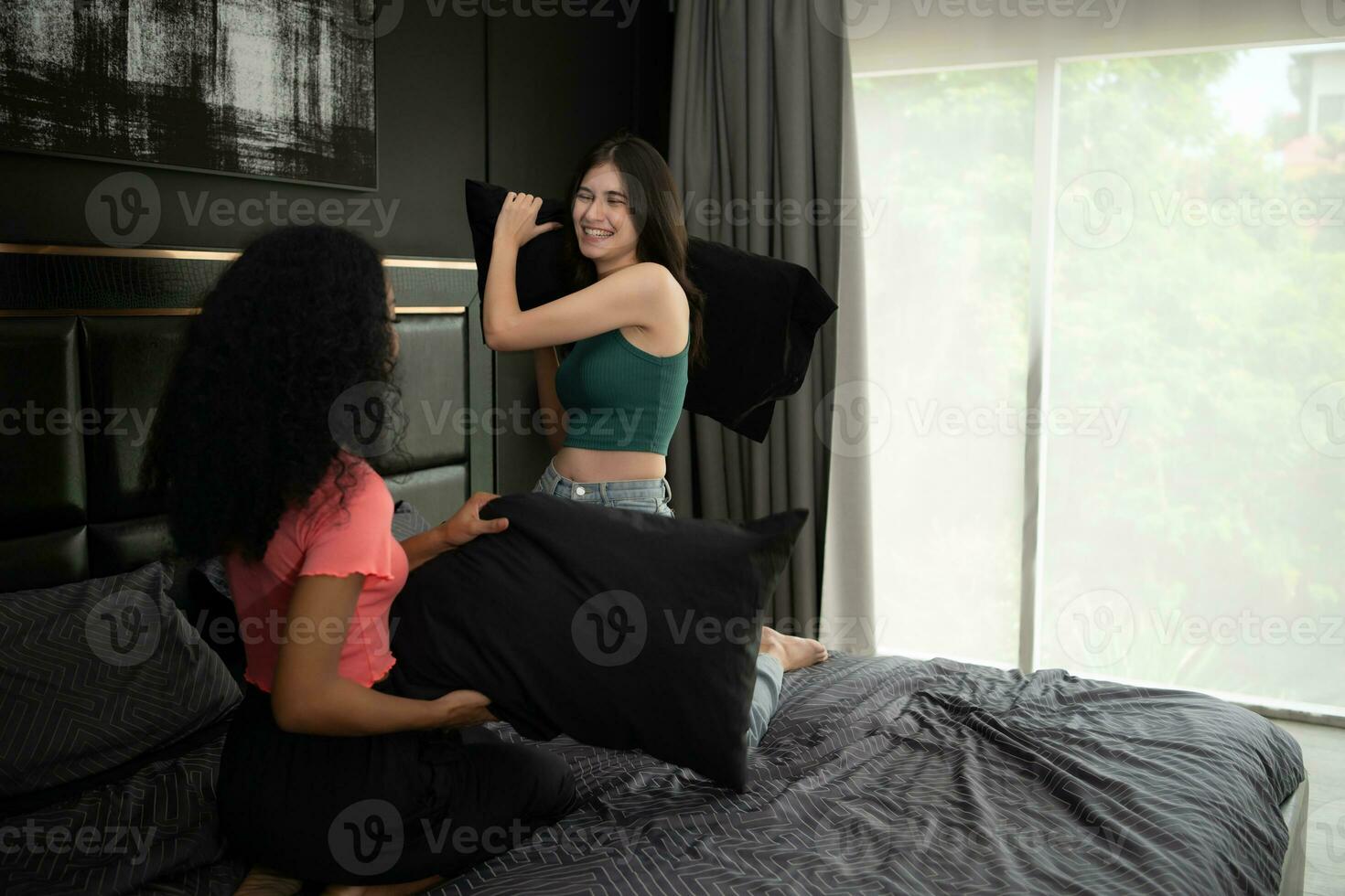 dois jovem mulheres jogar com almofadas em a cama dentro a quarto às lar. amizade e estilo de vida conceito. foto