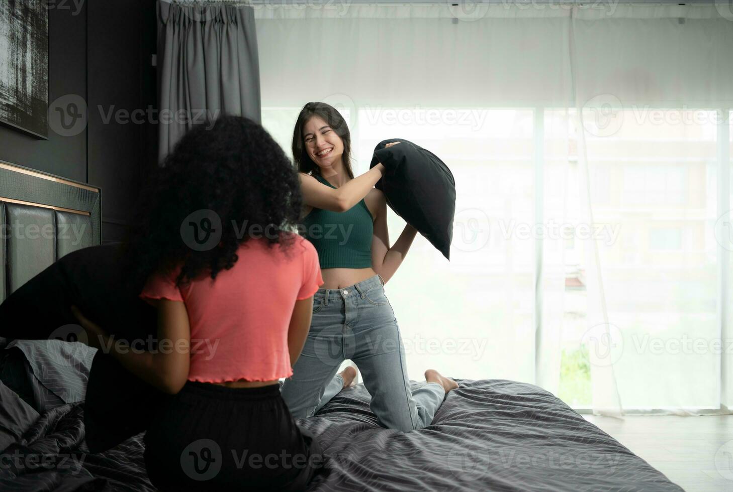 dois jovem mulheres jogar com almofadas em a cama dentro a quarto às lar. amizade e estilo de vida conceito. foto