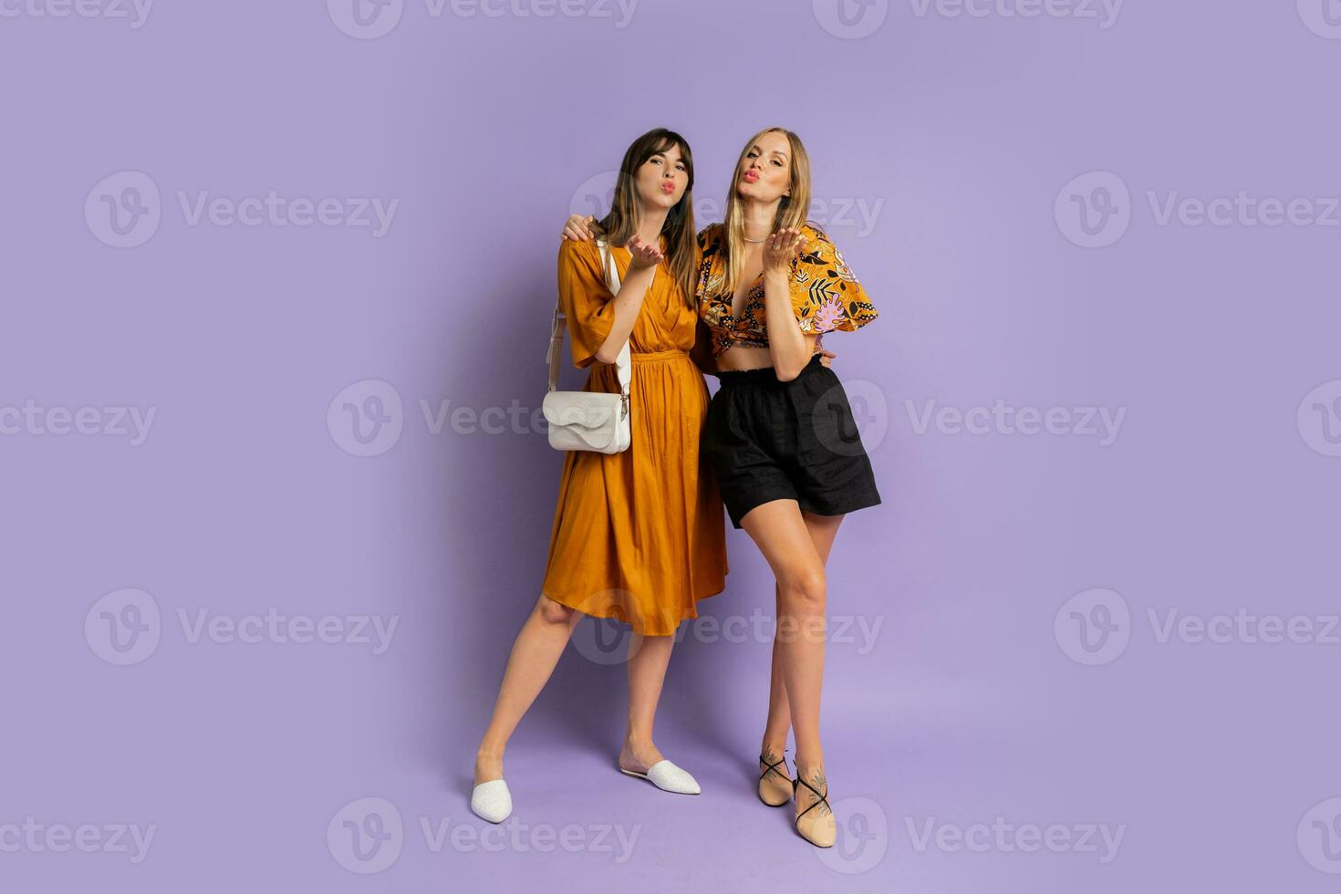 dois elegante europeu mulheres posando dentro estúdio sobre roxa fundo. vestindo à moda verão roupa. cheio comprimento. foto