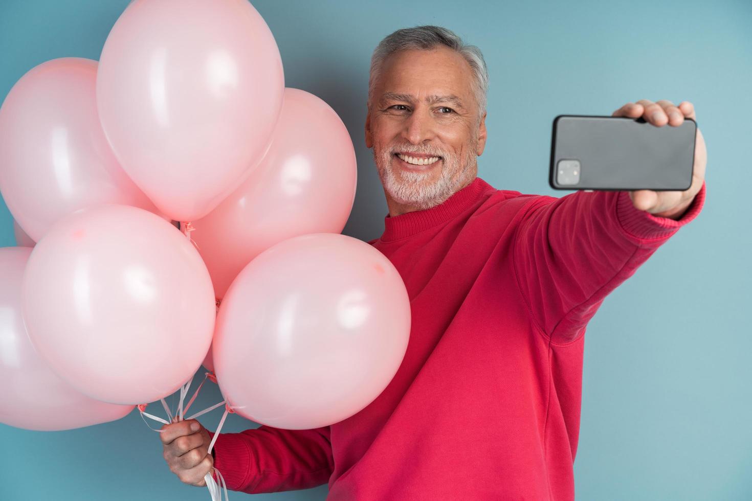 homem alegre, sorridente, de cabelos grisalhos e bolas em um fundo azul foto