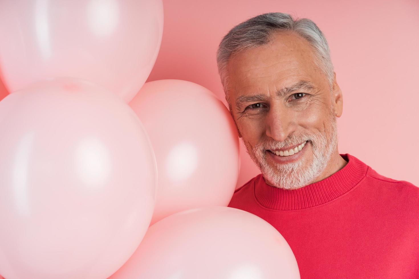 homem sênior com cabelos grisalhos, barba e balões cor de rosa foto