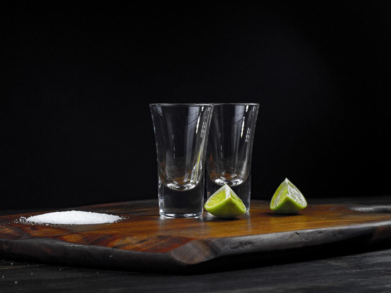 duas doses de tequila vazias com limão e sal marinho em uma placa de madeira foto