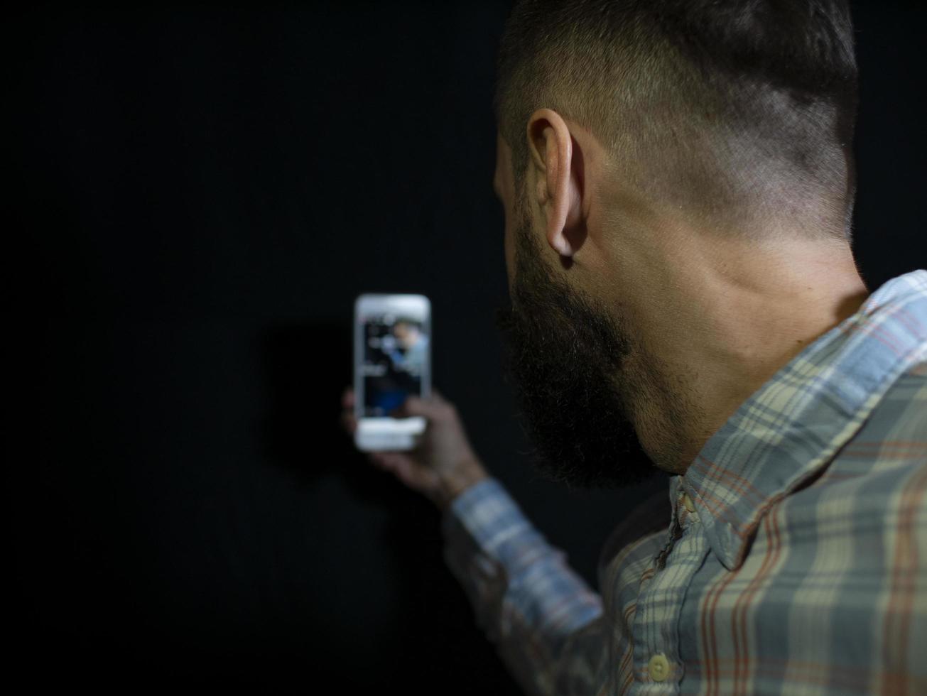 homem com barba e bigode olha para o telefone e faz uma selfie foto