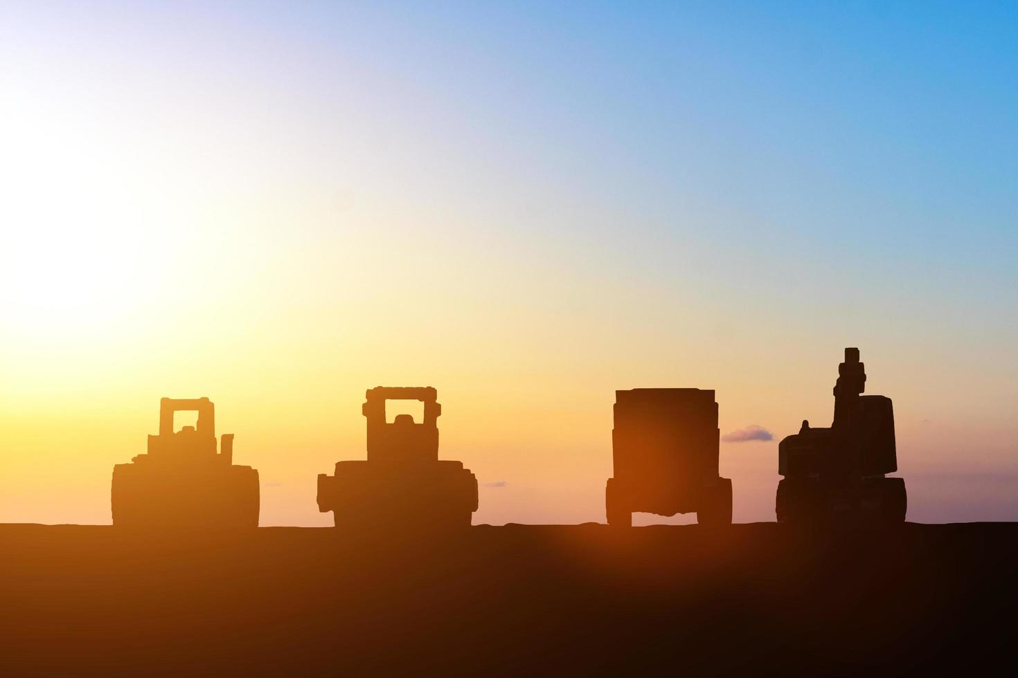 silhueta de escavadeira e caminhão no canteiro de obras ao pôr do sol foto