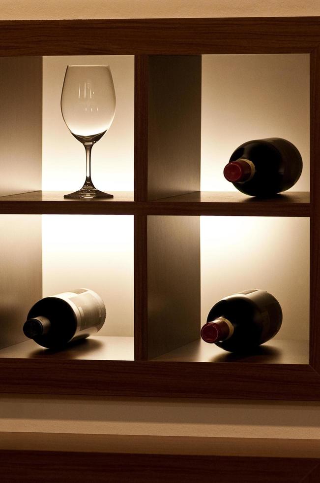 uma taça de vinho vazia e três garrafas na prateleira foto