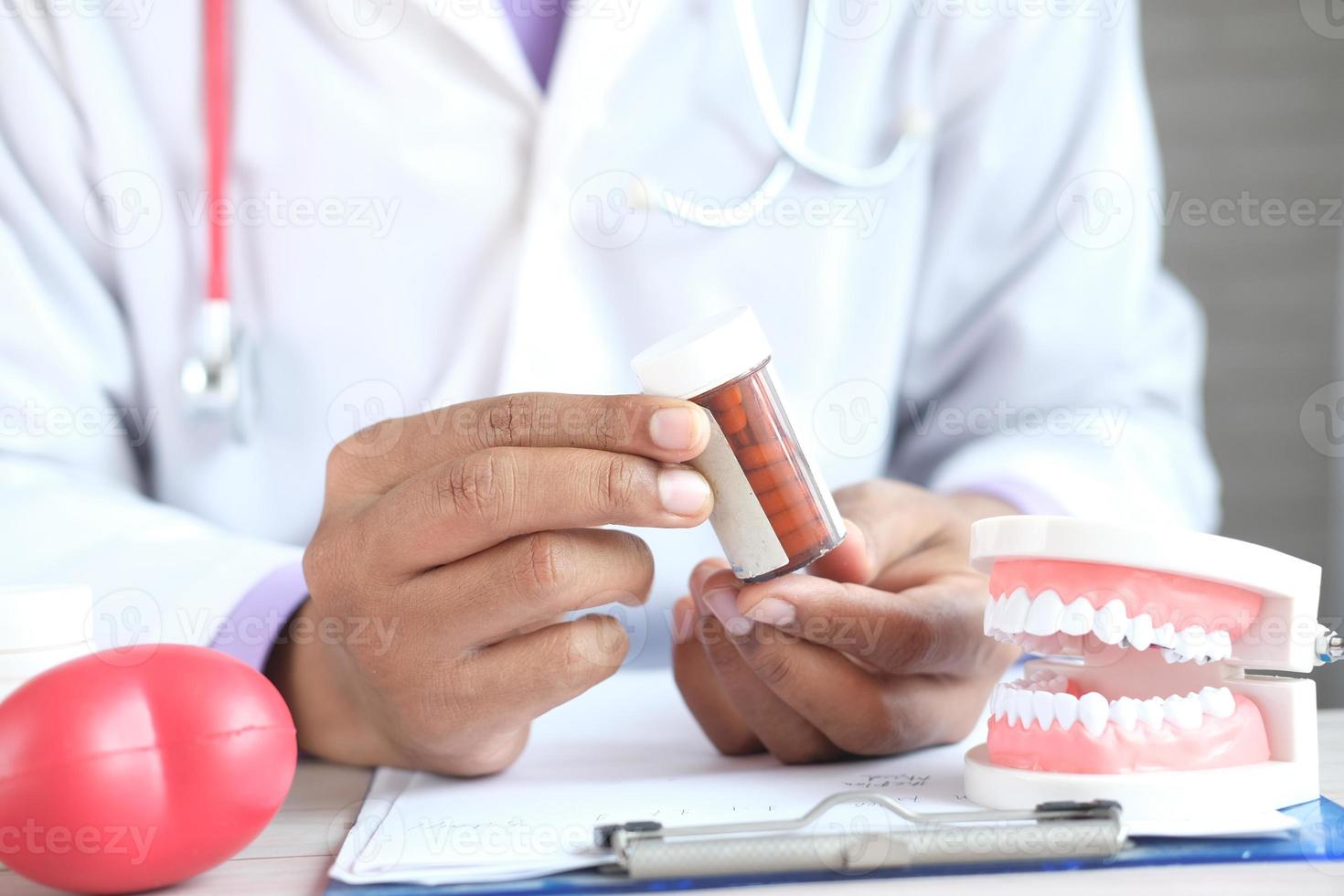 médico segurando o frasco de comprimidos e o modelo de dente dentário de plástico na mesa foto