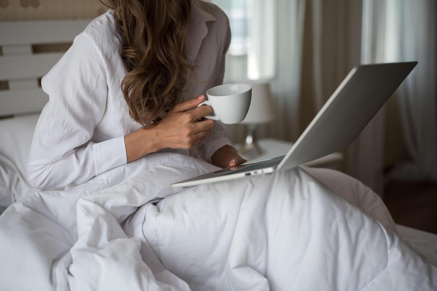 mulher bonita feliz trabalhando em um laptop na cama da casa foto