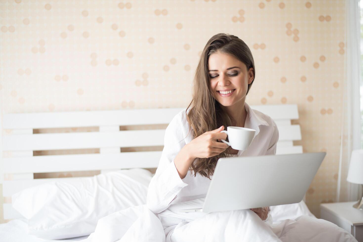 mulher bonita feliz trabalhando em um laptop na cama da casa foto