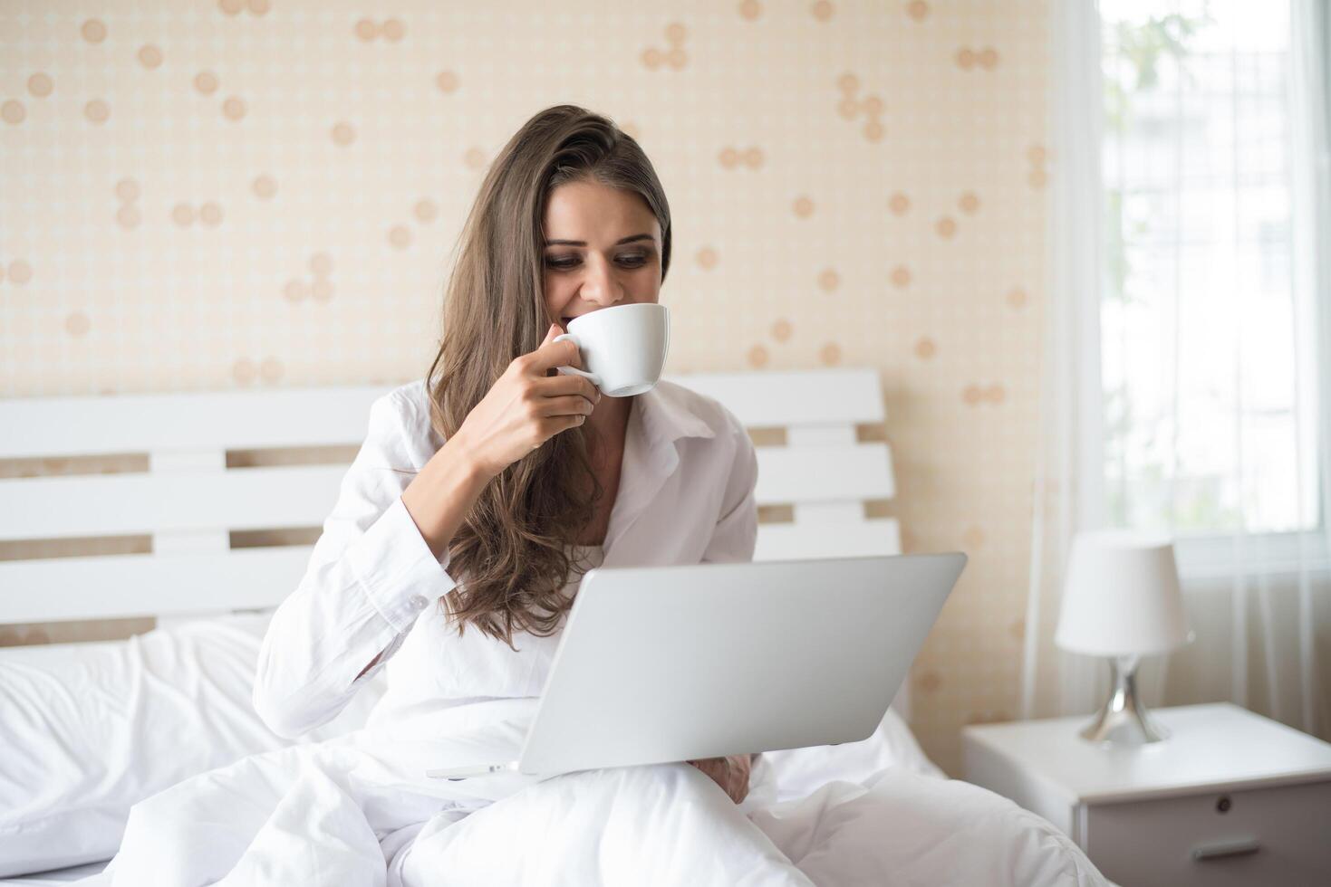 mulher bonita feliz trabalhando em um laptop na cama da casa foto