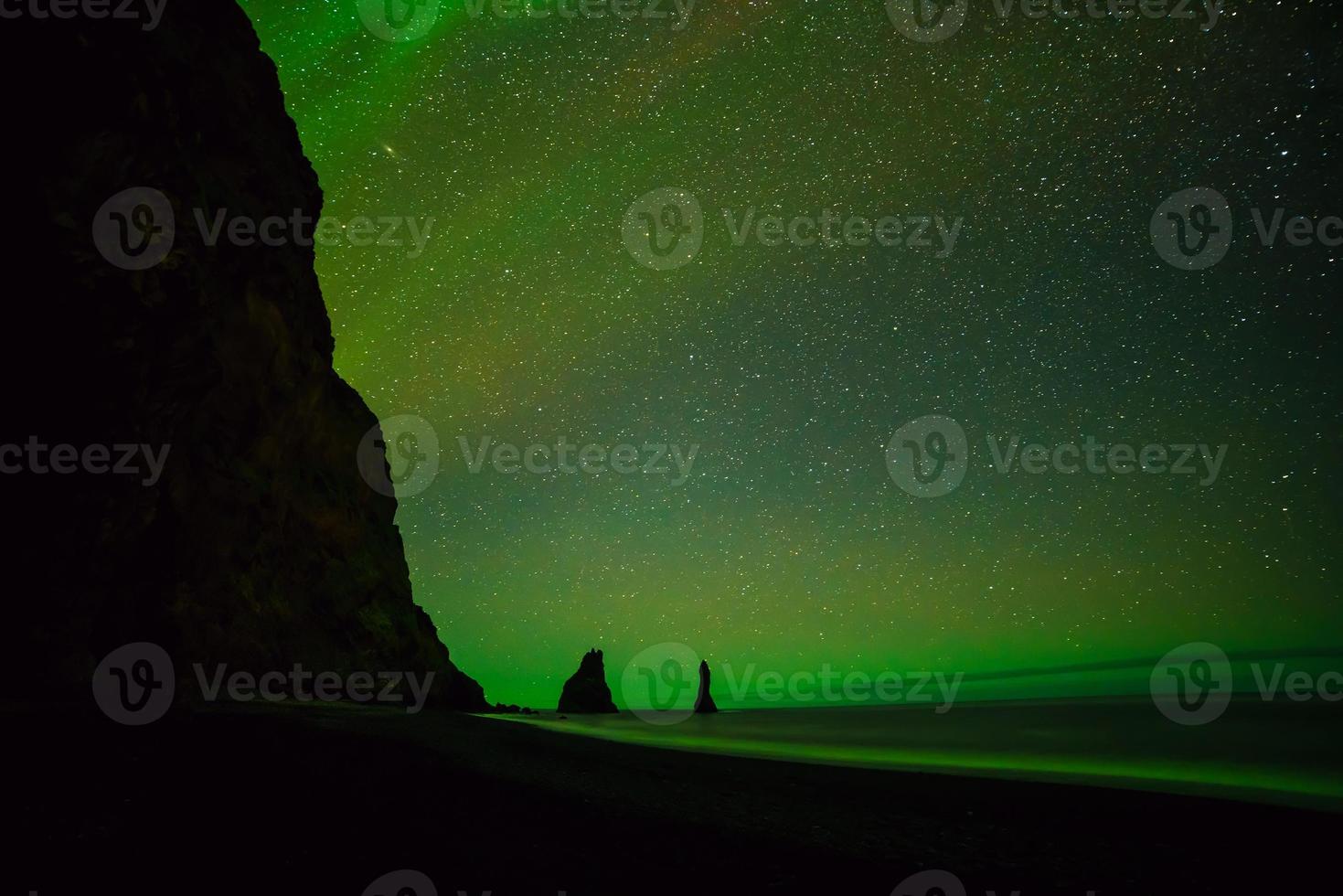 aurora boreal acima da praia de areia preta em vik foto