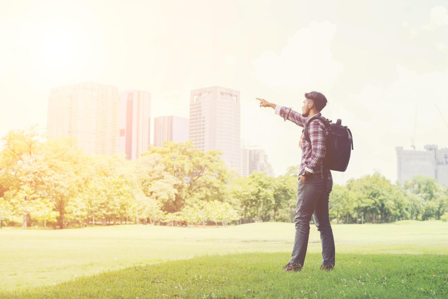 jovem hippie apontando para a vista da cidade do parque enquanto mochila foto