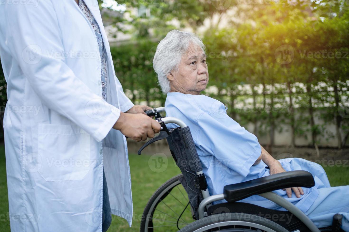 médico ajuda paciente idosa asiática sentada em cadeira de rodas no parque foto