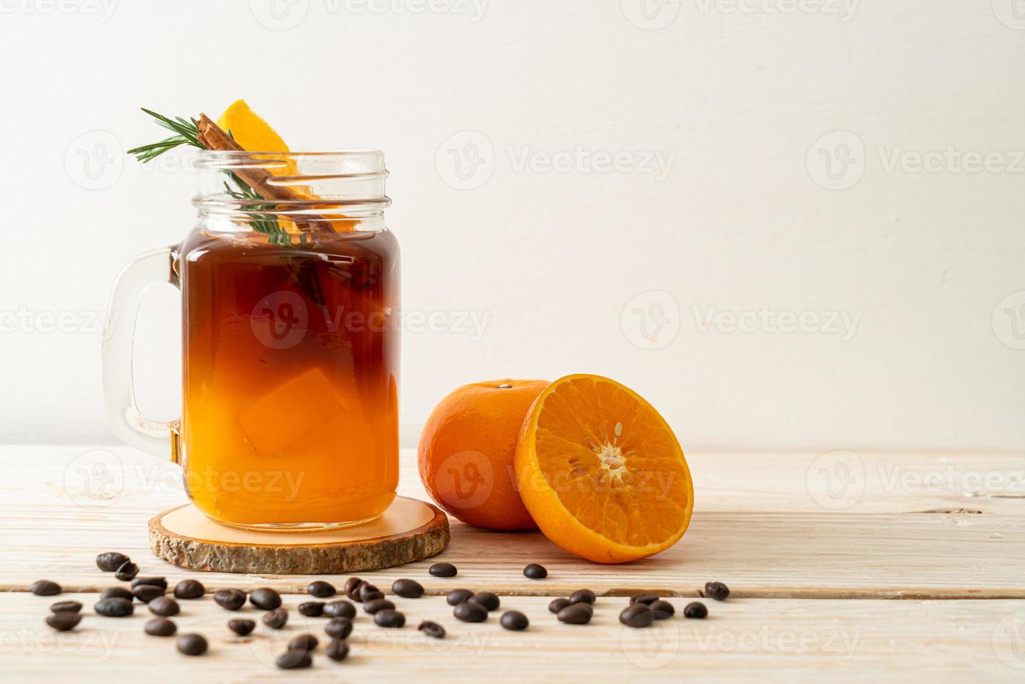 um copo de café preto americano gelado e uma camada de suco de laranja e limão decorado com alecrim e canela foto